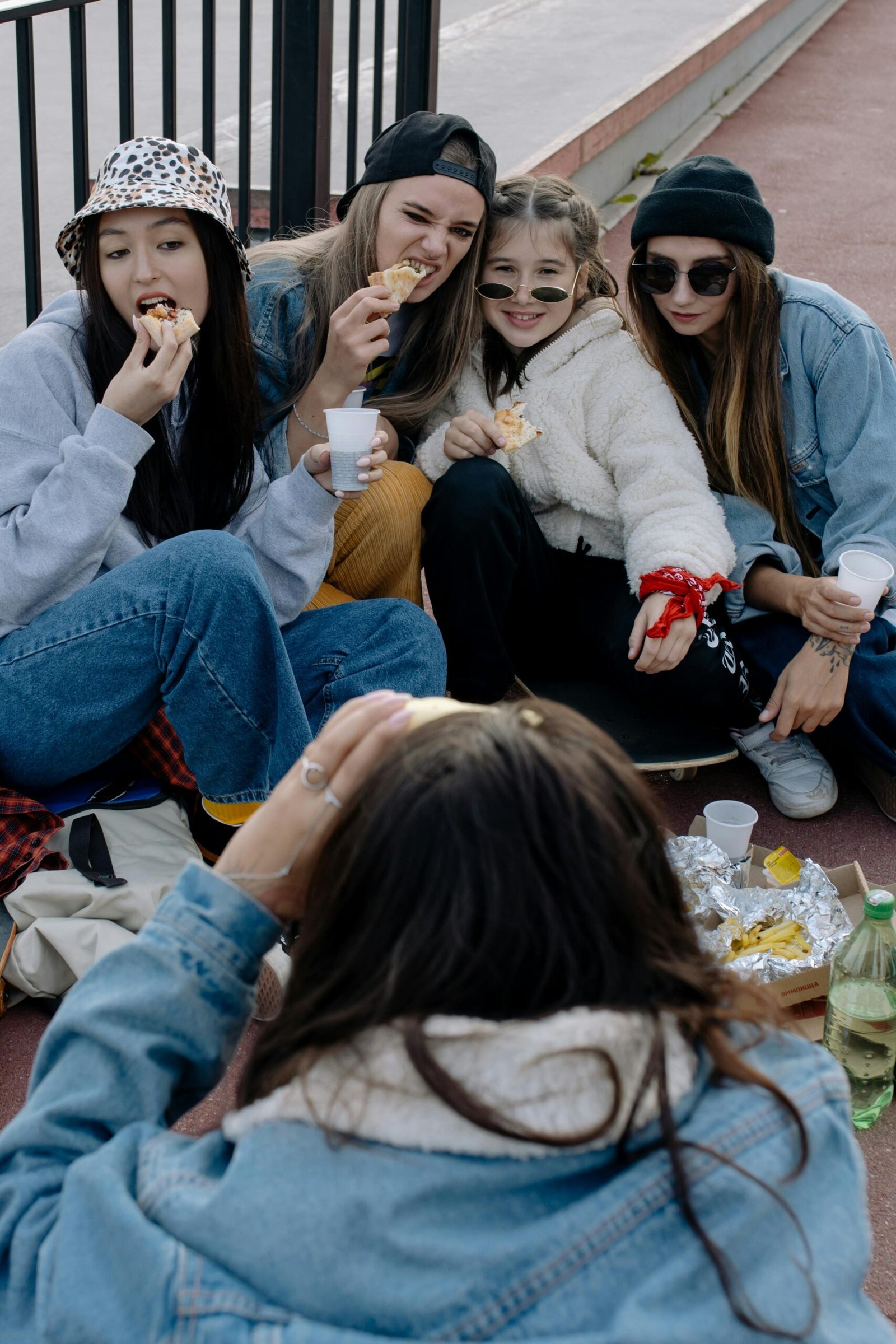 Home A group of trendy teenagers sitting outdoors, enjoying a casual lunch together.