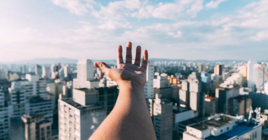 ¿Cómo se construyen las aspiraciones durante la adolescencia? An outstretched hand reaching towards a sunny cityscape, capturing the vibrant skyline and skyscrapers.