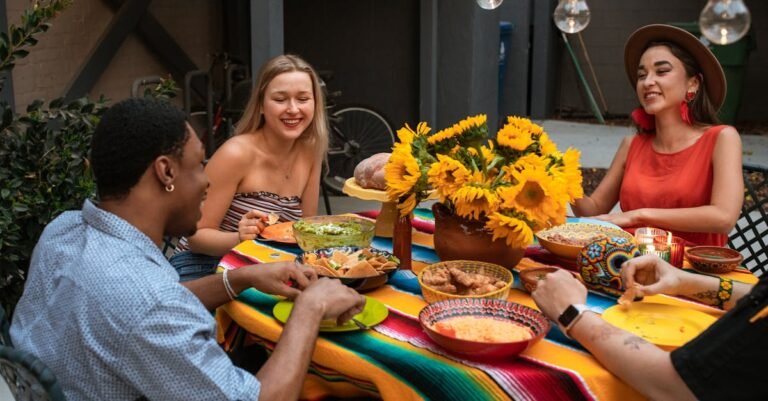 A group of friends enjoy a colorful meal outdoors with a sunflower centerpiece.