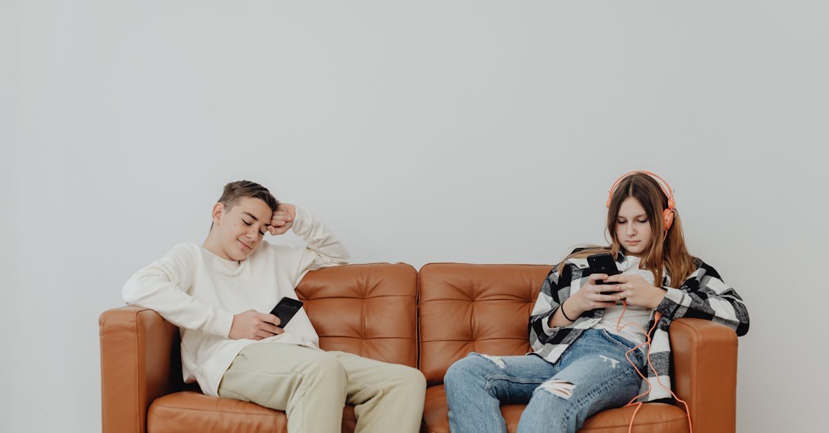 Teenagers lounging on a leather sofa using smartphones, displaying modern leisure.