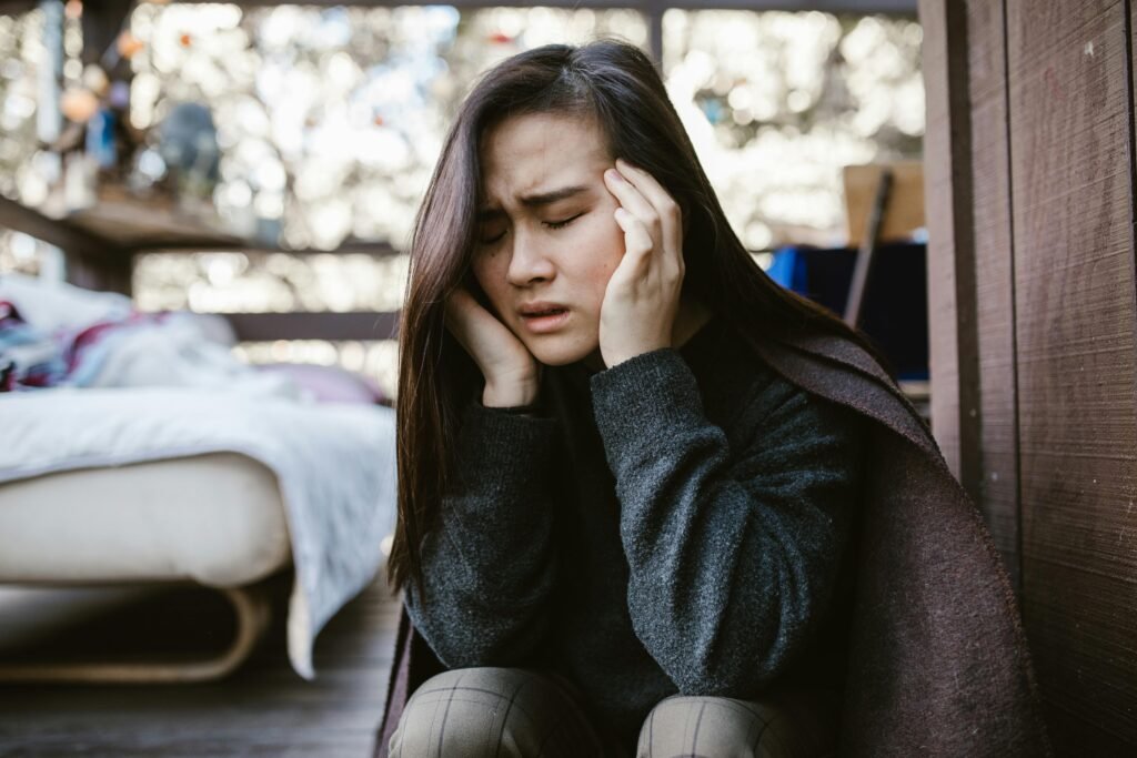 A young woman holds her head in distress while sitting indoors, capturing an emotional moment.
