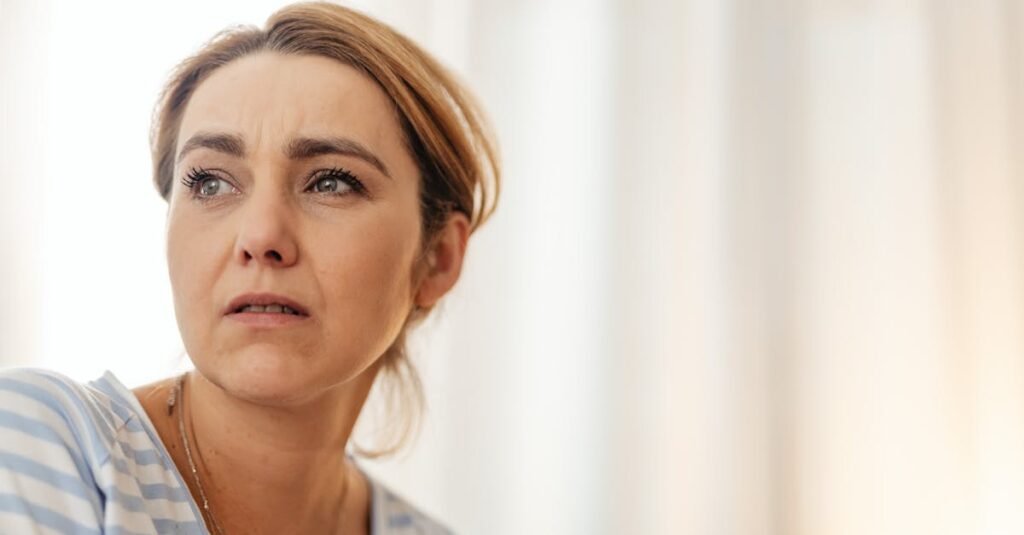 Thoughtful woman in striped shirt gazing away in gentle indoor lighting.
