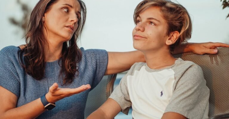 A mother and her teenage son engage in a conversation sitting outside, expressing familial warmth and connection.