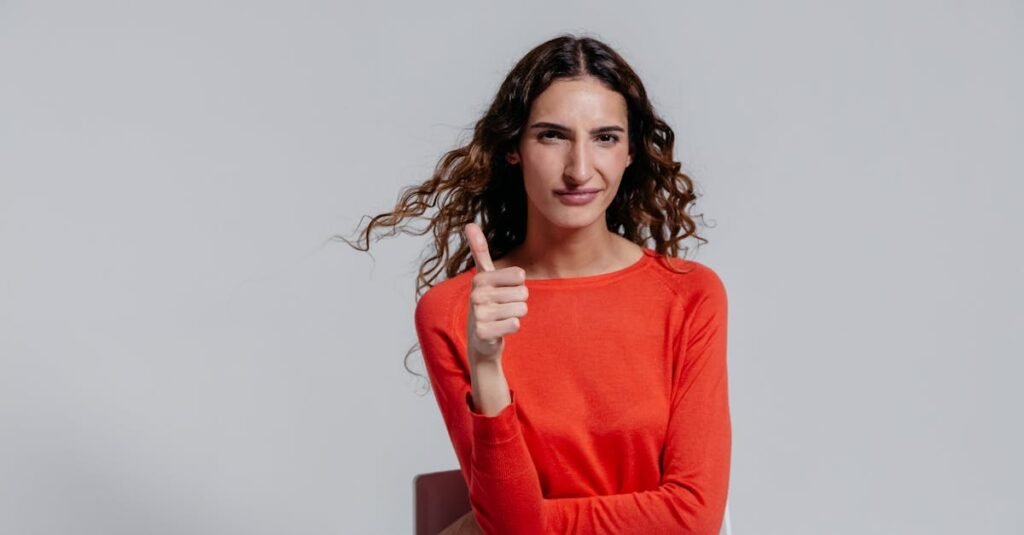 Confident woman in a red dress showing a thumbs up gesture indoors.