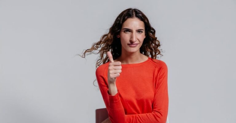 Confident woman in a red dress showing a thumbs up gesture indoors.