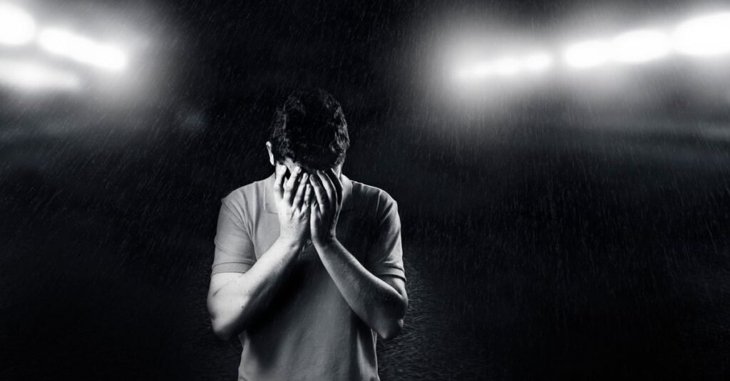 Black and white photo of a man covering his face, conveying emotion and solitude.