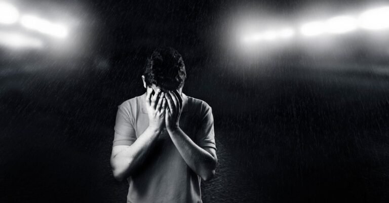 Black and white photo of a man covering his face, conveying emotion and solitude.