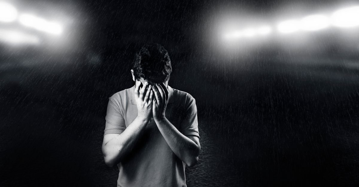 Black and white photo of a man covering his face, conveying emotion and solitude.